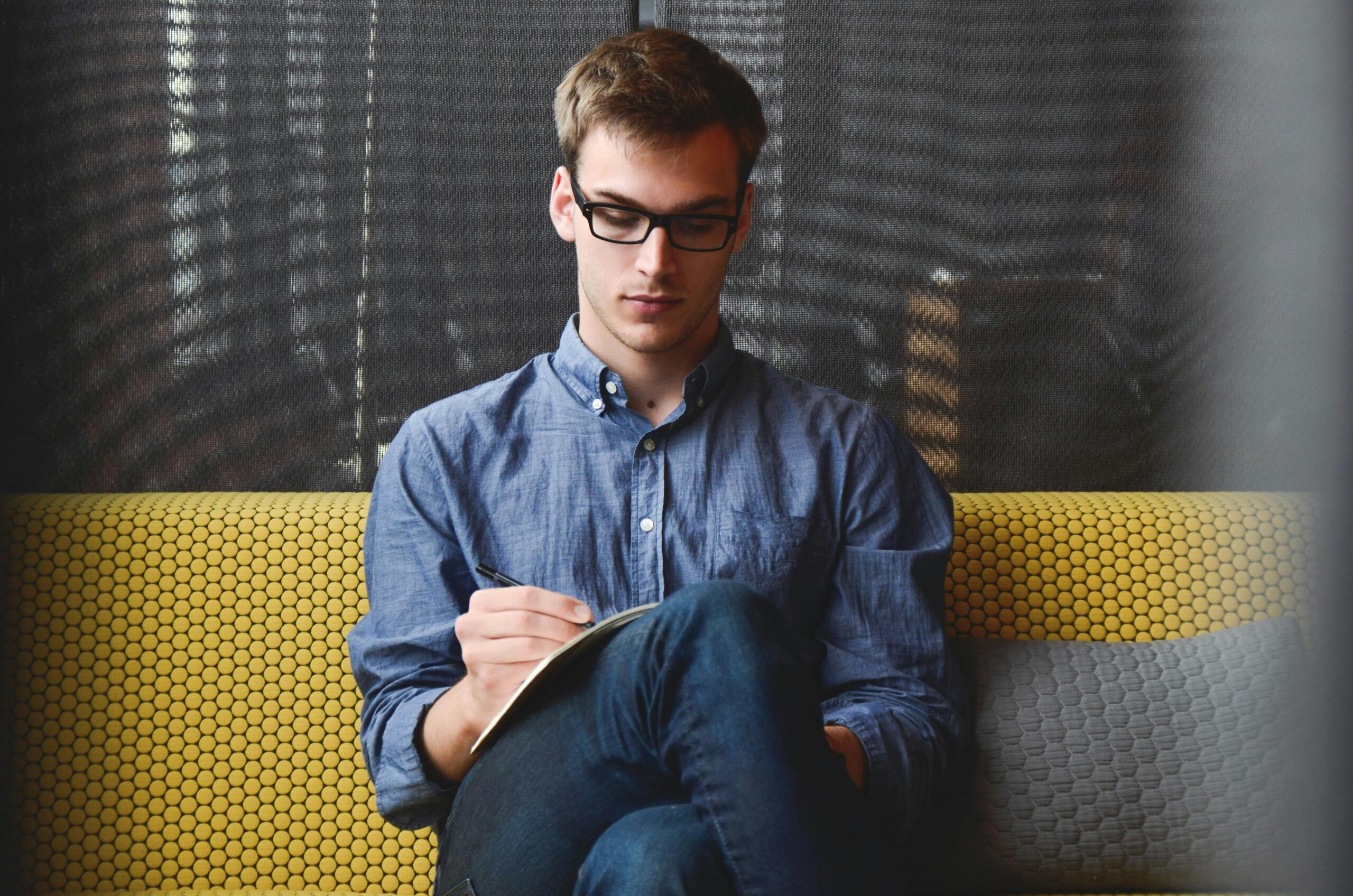Young man in glasses writes in a notebook.