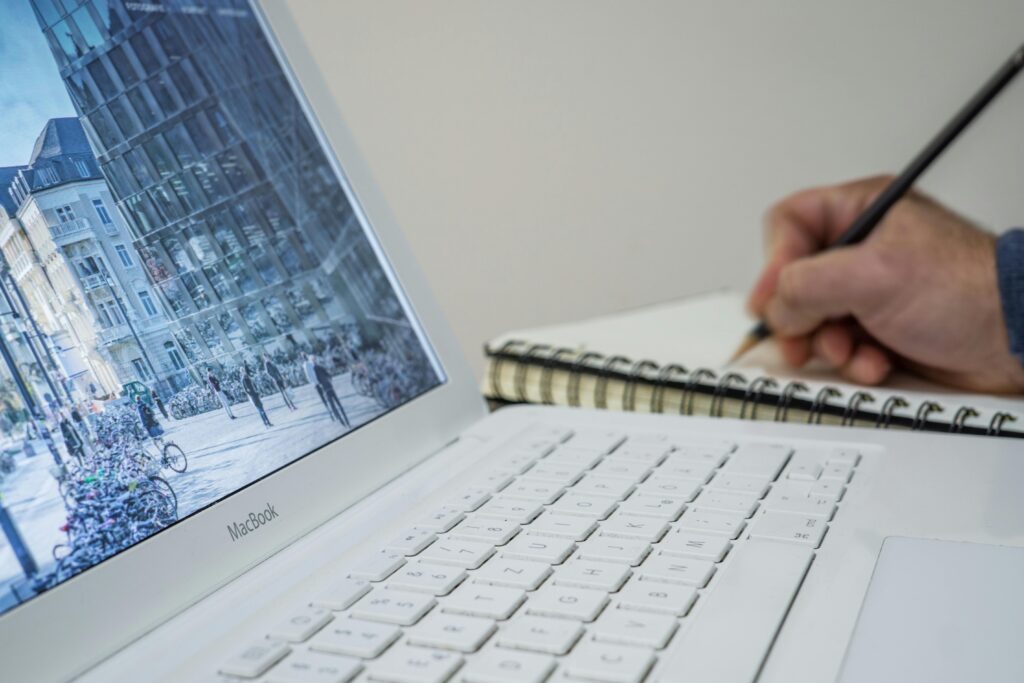 A person taking notes in a notebook beside an open laptop displaying an urban scene.Bring to a Job Interview