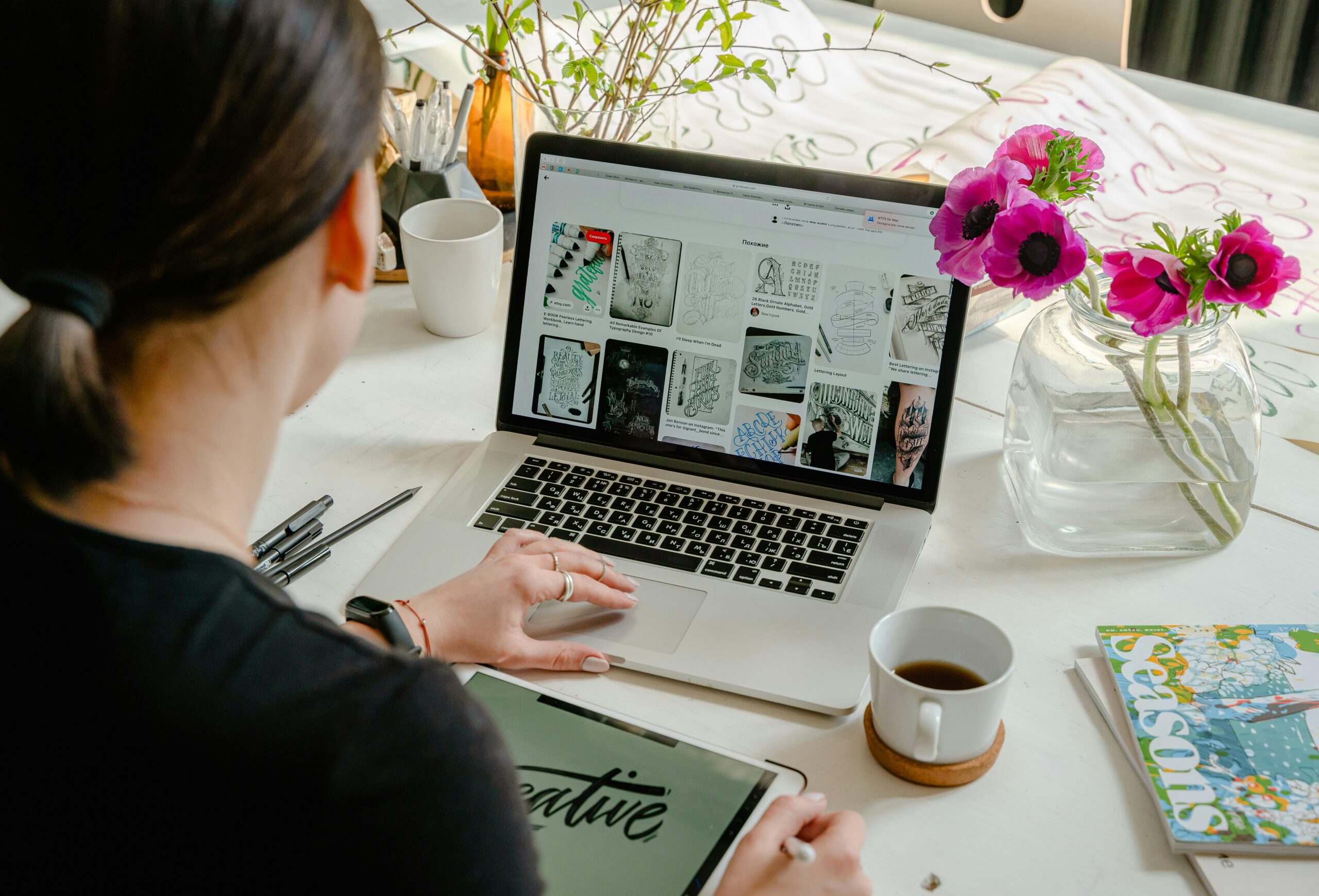 Woman using laptop and tablet in a creative workspace, calligraphy tools nearby. Artistic and tech-driven.