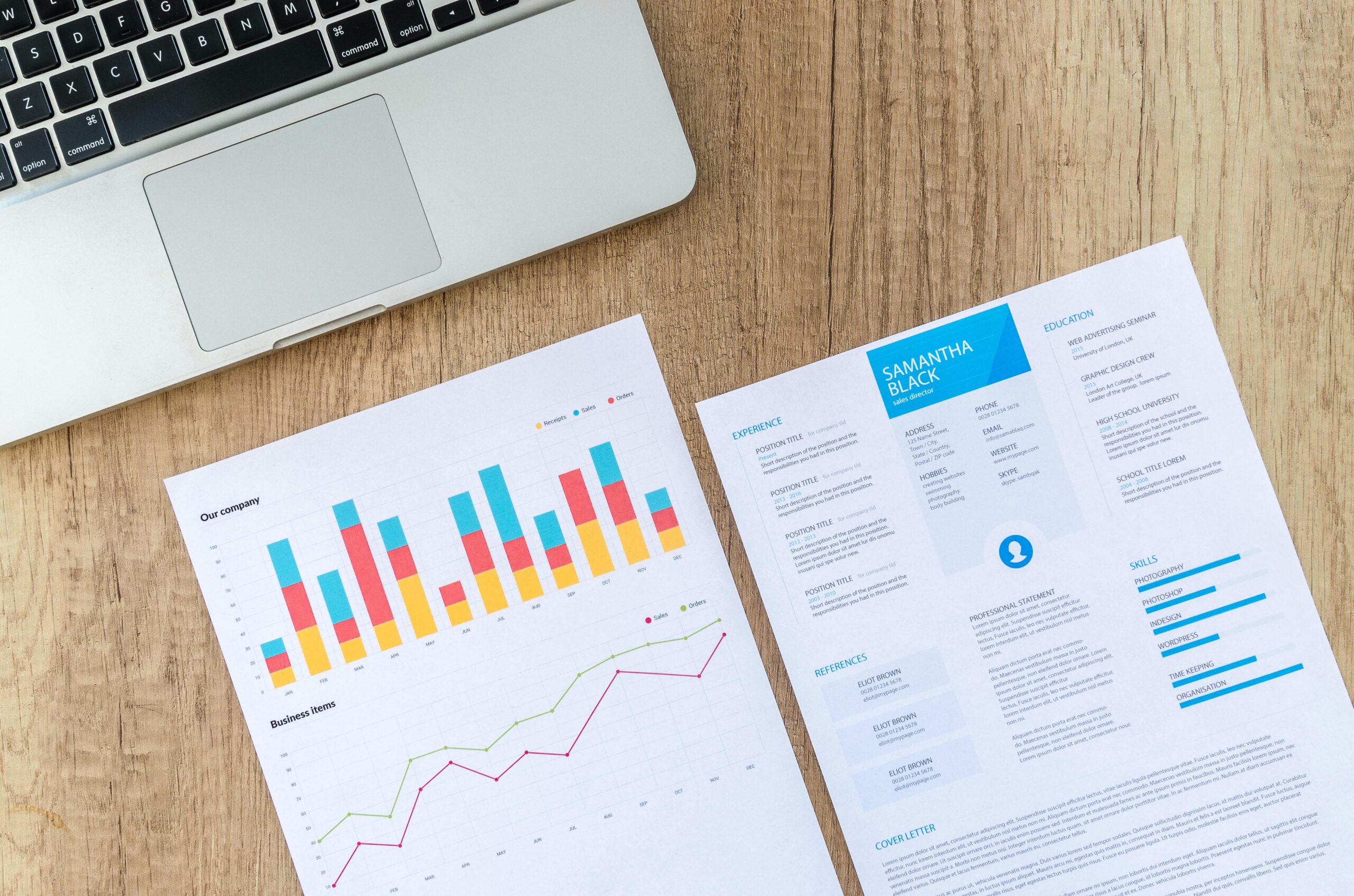 Laptop, charts, & resume on a wooden desk: business analysis & job application.