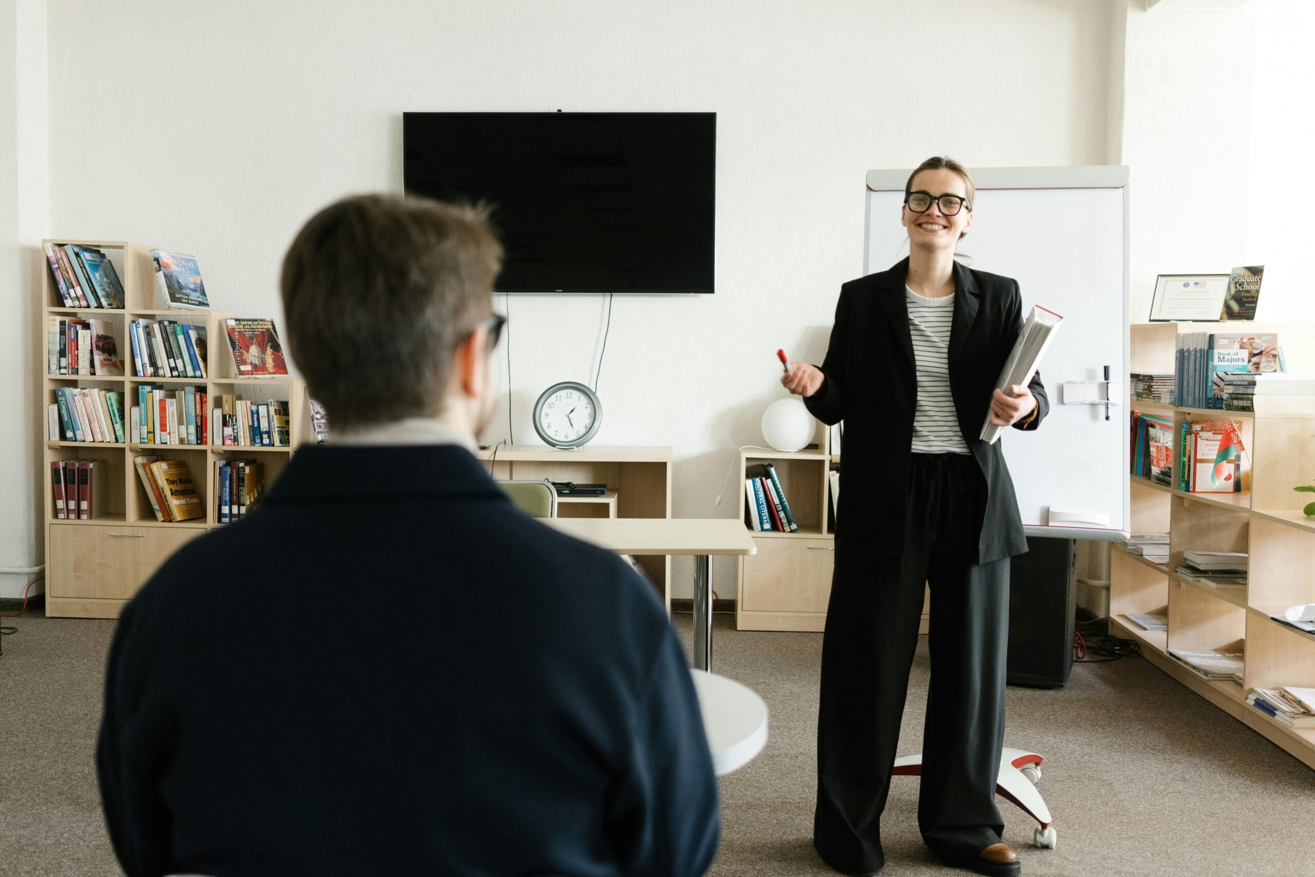 Businesswoman giving presentation in modern office with bookshelves and clock.