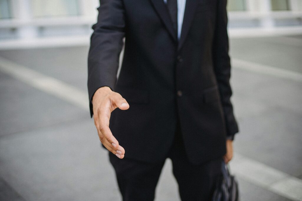 Close-up of a businessman in a suit reaching out for a handshake, symbolizing connection.